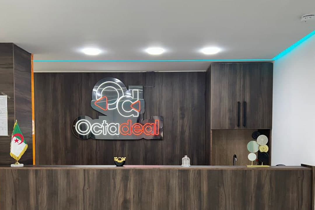 L'accueil de l'agence Octadeal à Tizi Ouzou : enseigne lumineuse Octadeal derrière le comptoir.